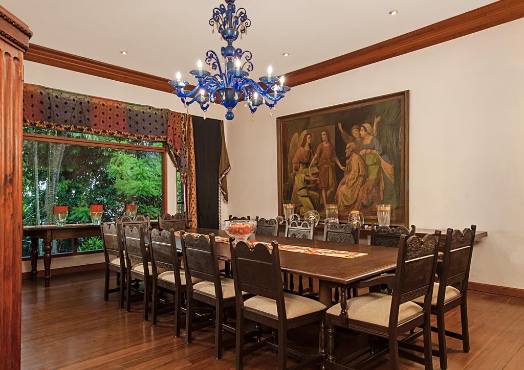 The dining room is dominated by the long Spanish table and antique chairs, paired with a blue Murano chandelier and Nikki's collection of folk fabrics used as curtain hangers. The large painting is by a Spanish artist and dates back to the 1880s.