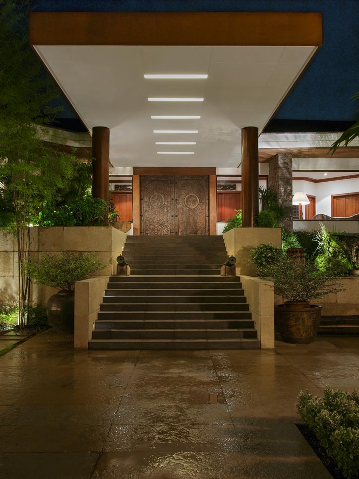 Courtyard view of the refurbished grand entrance. Calma removed the original driveway that ended at the porte-cochere, and substituted it with two flights of stone-covered stairs with monumental stereobates beneath the original concrete canopy, which is dressed in wooden pillars. 